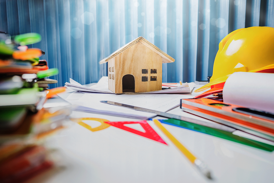 Model home surrounded by hardhat and planning tools.