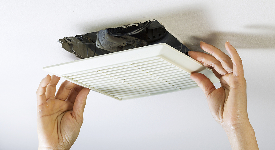 Hands removing a bathroom fan from the ceiling.