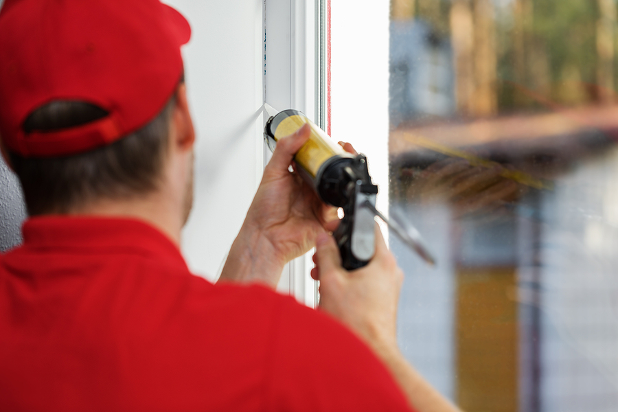 Worker applying caulk around window frame as part of air sealing.