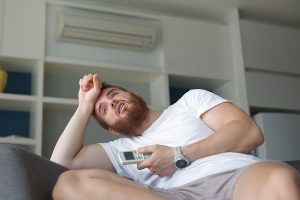 Young homeowner with AC remote overheating inside their home.