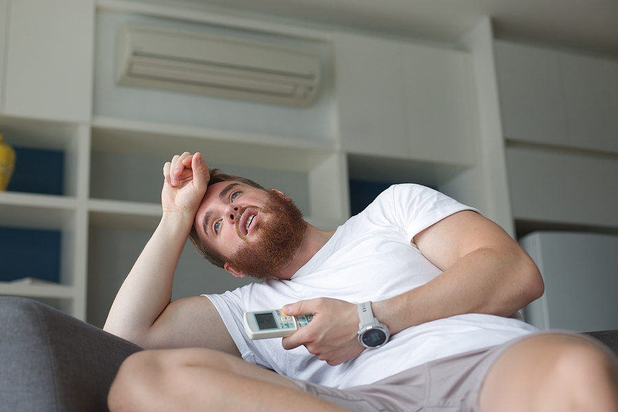 Young homeowner with AC remote overheating inside their home.
