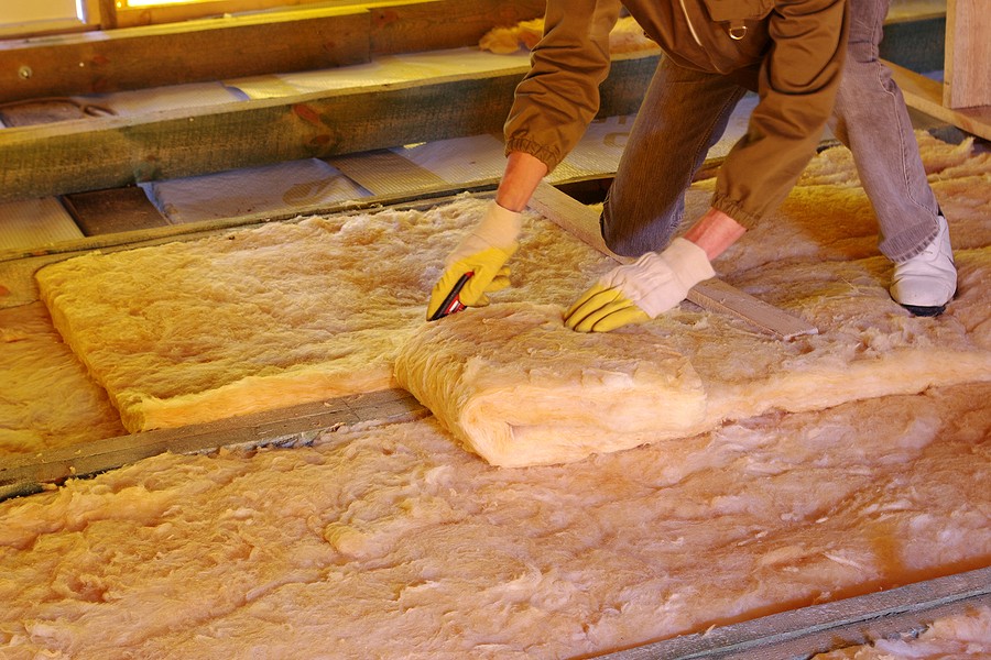 Worker installing insulation in an unfinished attic.