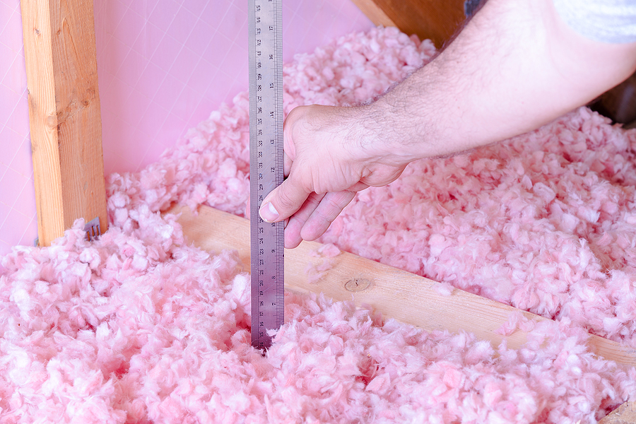 Insulation contractor measuring loose insulation depth in attic.