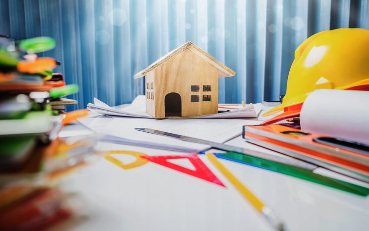 Model home surrounded by hardhat and planning tools.